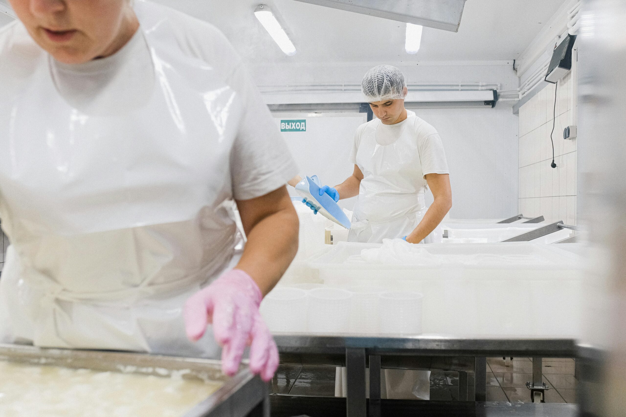Cheese factory workers in protective gear process dairy products indoors.
