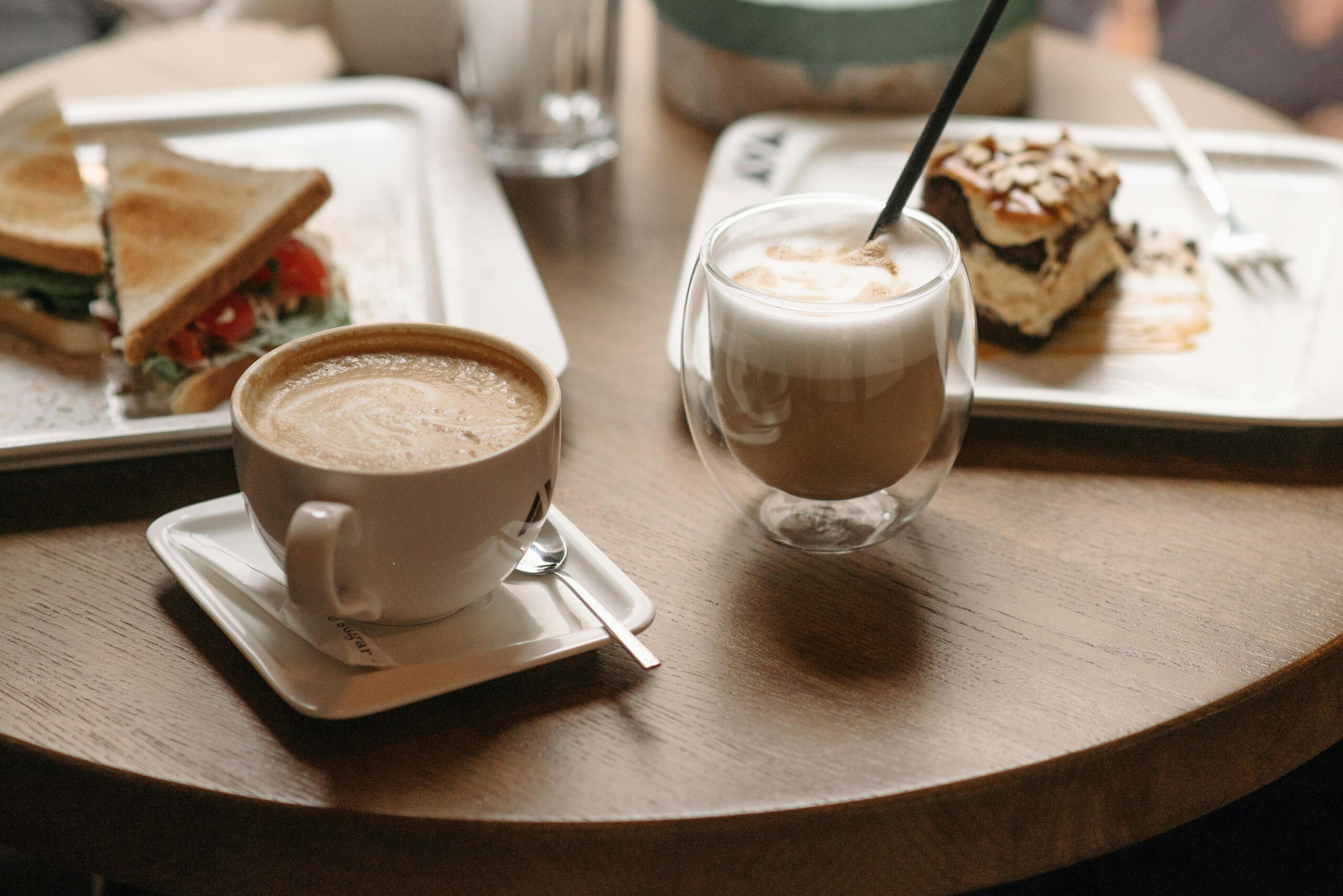 Inviting cafe table scene with a cup of coffee, fresh sandwich, and dessert.